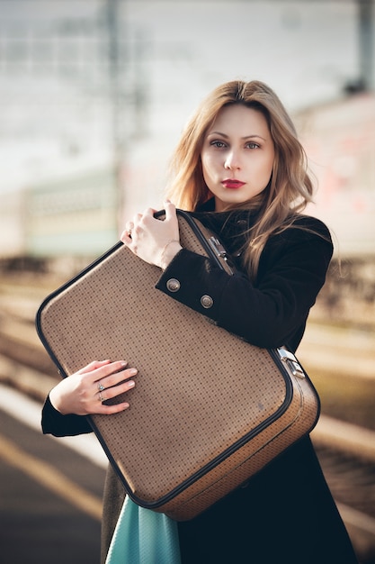 Ragazza bionda con una valigia in attesa di un treno alla stazione.