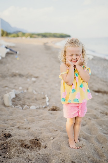 ragazza bionda dai capelli ricci che gioca su una spiaggia sabbiosa di ciottoli