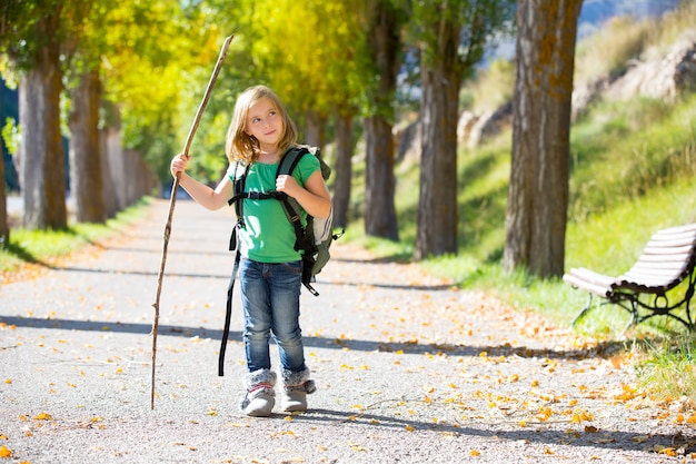 Ragazza bionda del bambino dell&#39;esploratore che cammina con lo zaino negli alberi di autunno