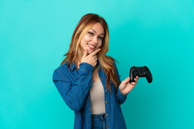 Ragazza bionda dell'adolescente che gioca con un controller per videogiochi su un muro isolato felice e sorridente