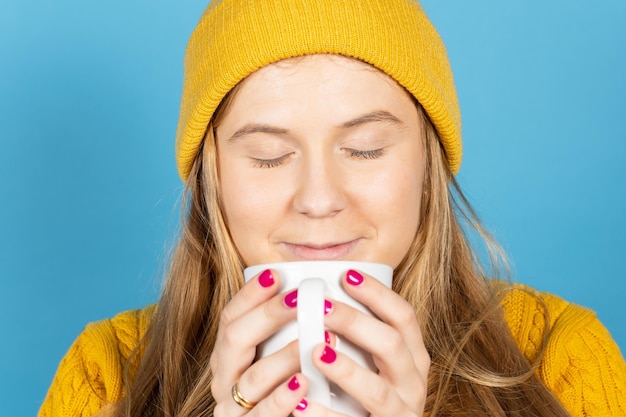 Ragazza bionda dell'adolescente che sente l'odore della tazza di caffè