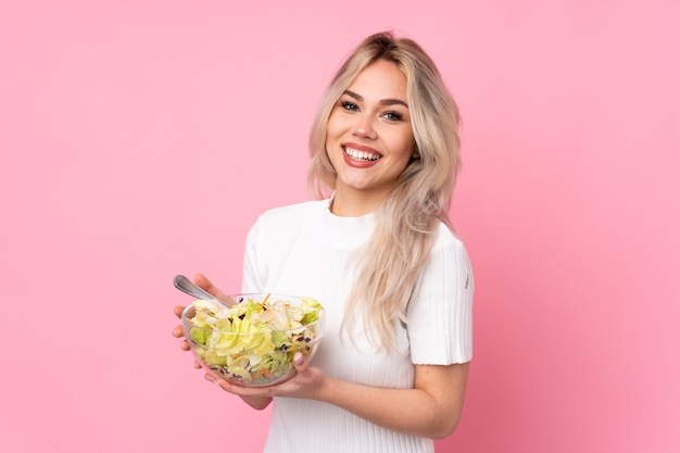 Ragazza bionda dell'adolescente che tiene un'insalata sopra la parete rosa isolata