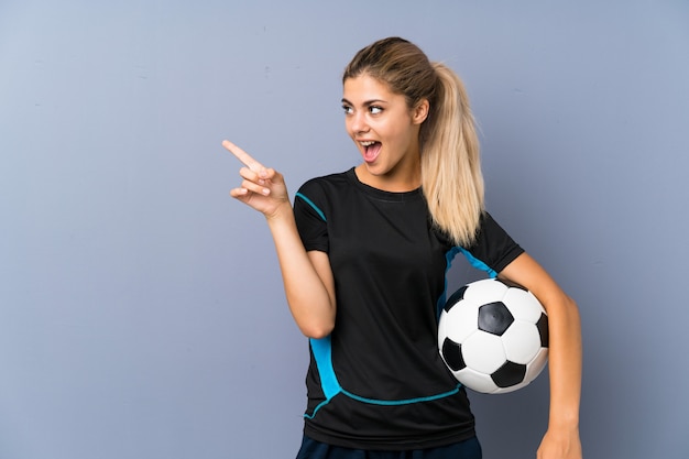 Ragazza bionda dell'adolescente del giocatore di football americano sorpresa e che indica dito il lato