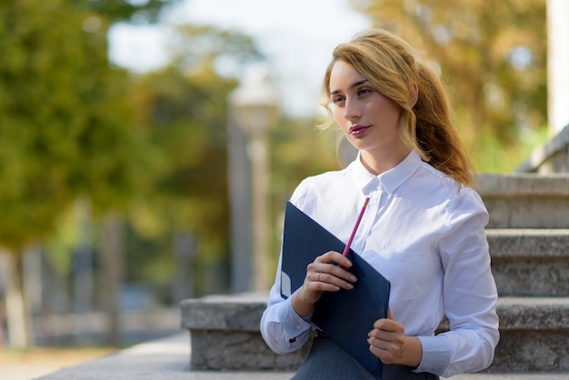 Ragazza bionda della scuola che pensa con una matita