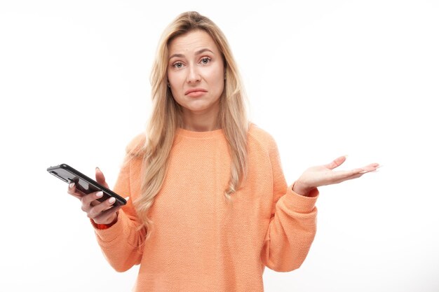 Ragazza bionda di pensiero pensierosa nello smartphone casuale della tenuta isolato sul fondo bianco dello studio