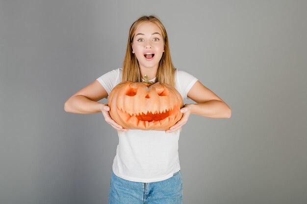 Ragazza bionda divertente allegra con la zucca della lanterna della presa o di Halloween isolata sopra grey