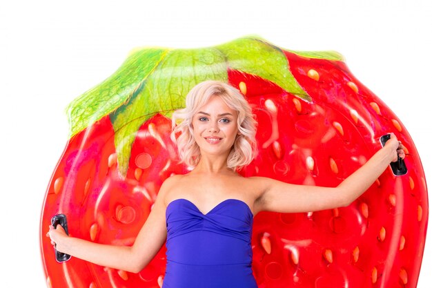 Ragazza bionda dolce in un costume da bagno blu sul materasso di nuoto della fragola