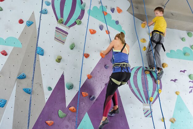 Ragazza bionda e scolaro afferrando da piccole rocce sull'attrezzatura da arrampicata durante l'allenamento nel centro ricreativo attivo