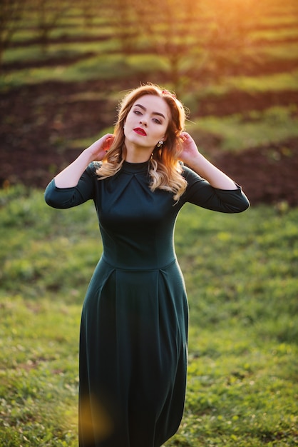 Ragazza bionda elegante di Yong al vestito verde sul giardino in primavera del tramonto.