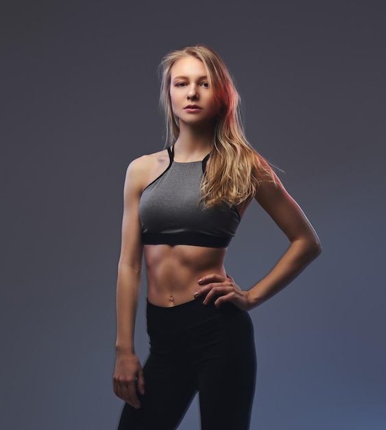 Ragazza bionda esile sexy in un abbigliamento sportivo in posa in uno studio. Isolato su sfondo grigio.