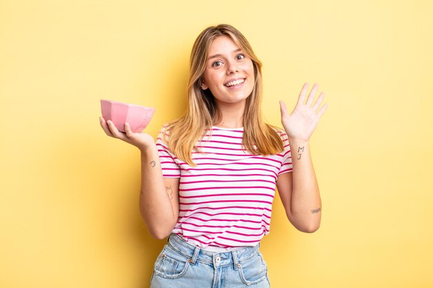 Ragazza bionda graziosa che sorride e che sembra amichevole, mostrando il numero cinque. concetto di ciotola vuota