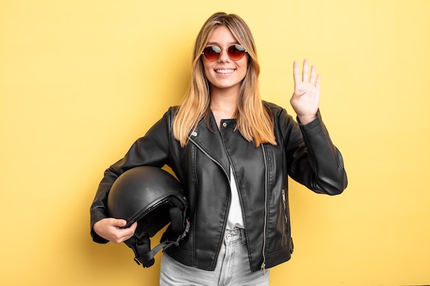 Ragazza bionda graziosa che sorride e che sembra amichevole, mostrando il numero quattro. concetto di casco da moto