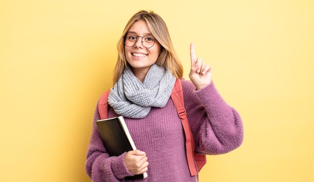 Ragazza bionda graziosa che sorride e che sembra amichevole, mostrando il numero uno. concetto di studente