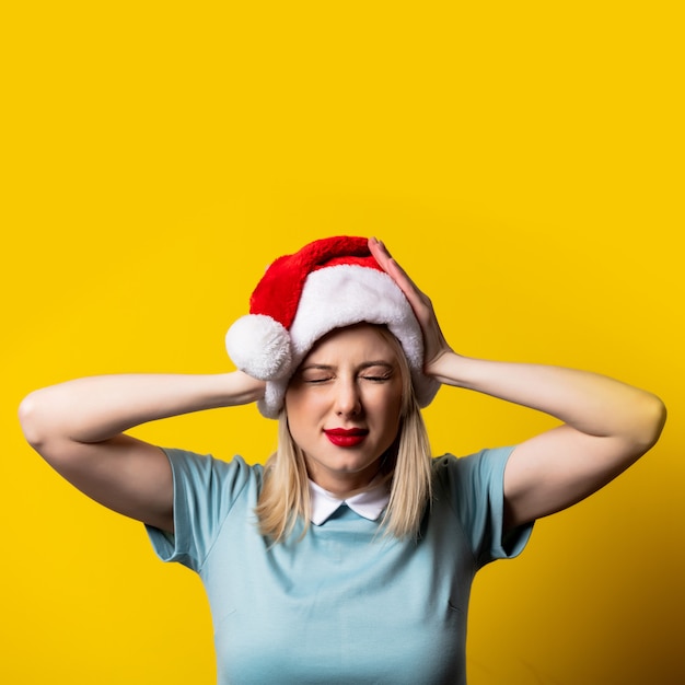 Ragazza bionda in abito blu e cappello di Babbo Natale sullo spazio giallo