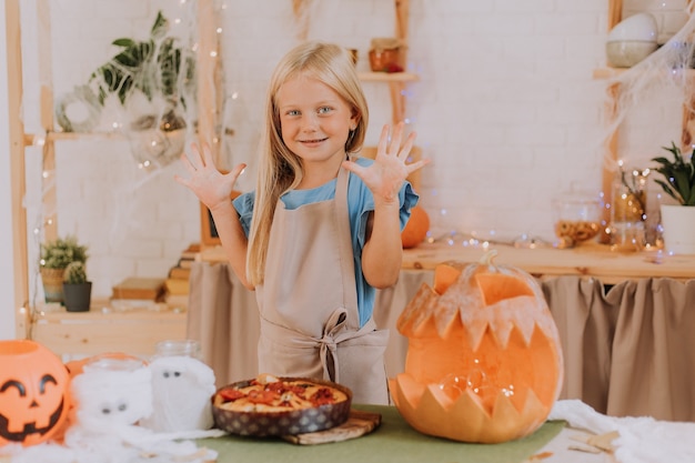 ragazza bionda in grembiule in cucina decorata con zucche per Halloween prepara una focaccia