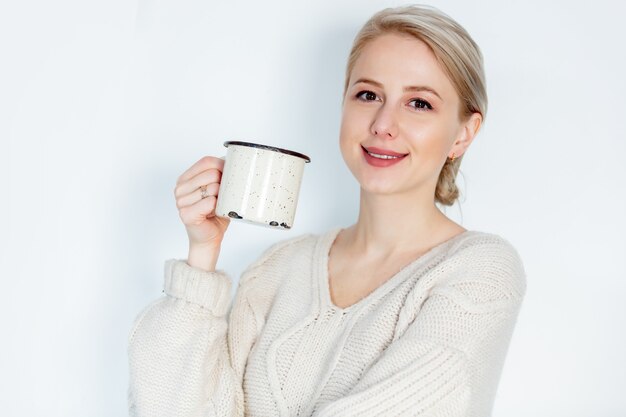 Ragazza bionda in maglione con la tazza su bianco