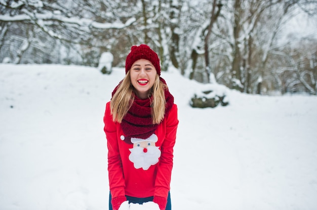 Ragazza bionda in maglione rosso sciarpa, cappello e Babbo Natale in posa al parco il giorno di inverno.