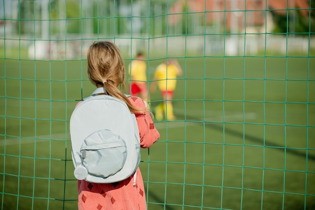 ragazza bionda in piedi vicino al campo di calcio e guardando giocare a calciatori calciatori