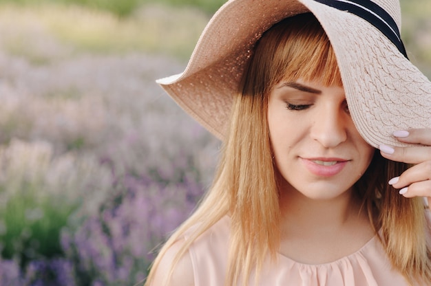 Ragazza bionda in un abito beige e cappello di paglia. Campo di lavanda