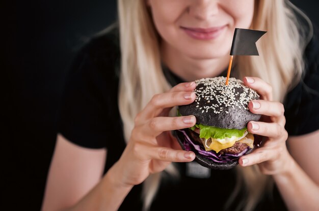 Ragazza bionda in una maglietta nera con un grande hamburger nero in mano