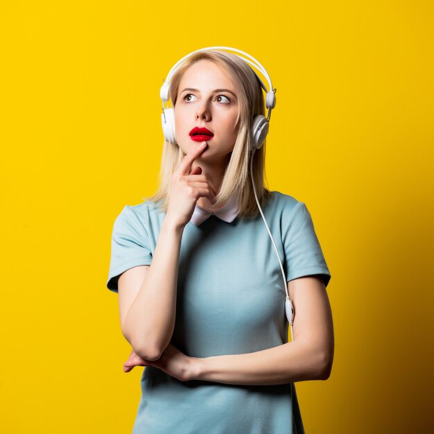 Ragazza bionda in vestito blu con le cuffie su spazio giallo