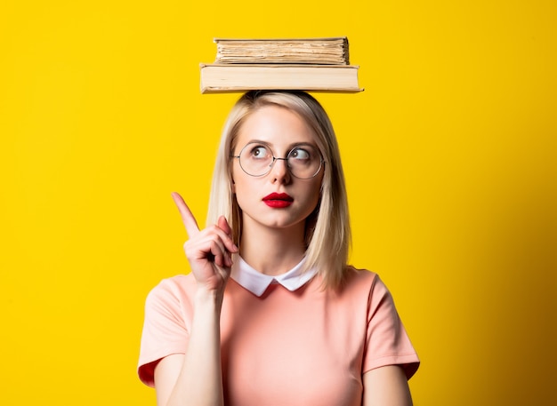 Ragazza bionda in vestito e vetri rosa con i libri su spazio giallo