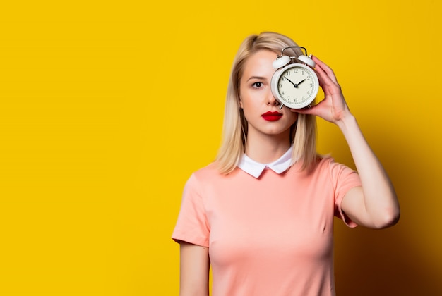 Ragazza bionda in vestito rosa con la sveglia su spazio giallo