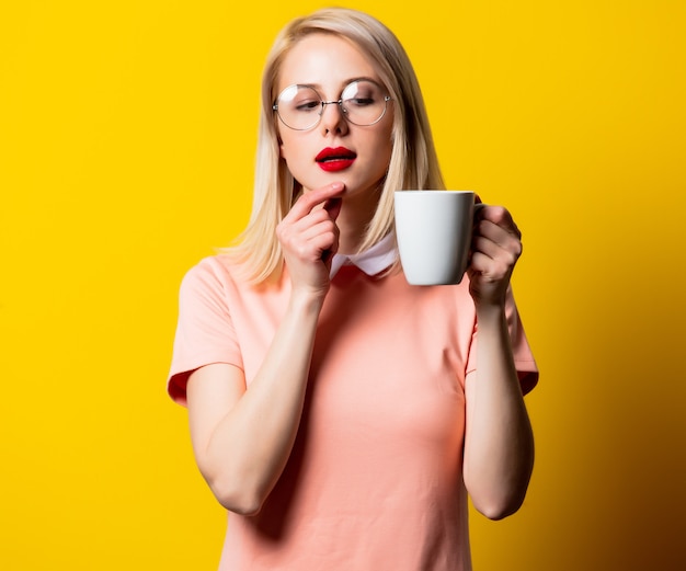 Ragazza bionda in vestito rosa con la tazza di caffè su spazio giallo