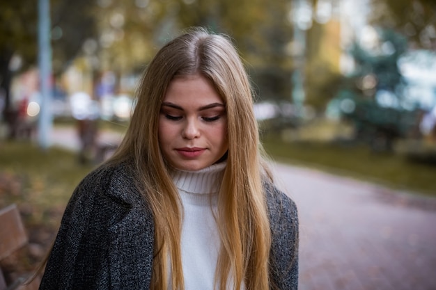 Ragazza bionda nella sosta di autunno si siede sulla panchina