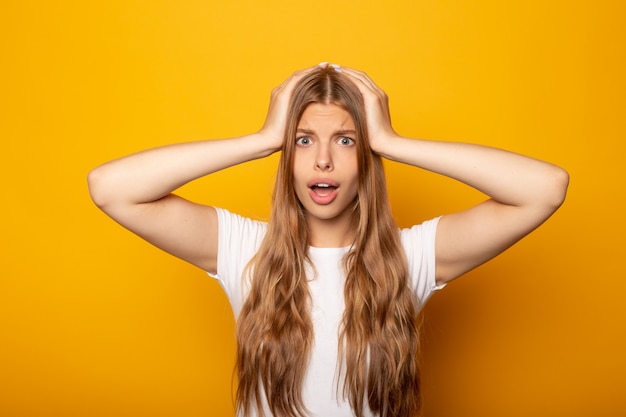 ragazza bionda pazza con la bocca commovente della bocca aperta isolata su giallo