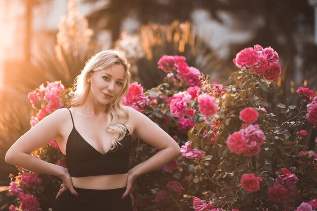 Ragazza bionda sorridente che posa sopra le rose all'aperto