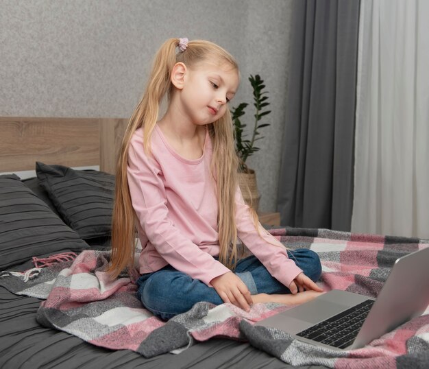 Ragazza bionda studia a casa online con un laptop a letto