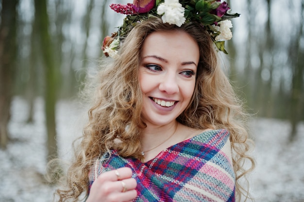 Ragazza bionda sveglia riccia con la corona in plaid a quadretti alla foresta nevosa nel giorno di inverno.