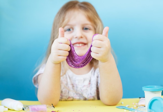 Ragazza bionda tenere la melma viola isolata su sfondo blu bambino che gioca con il giocattolo della melma