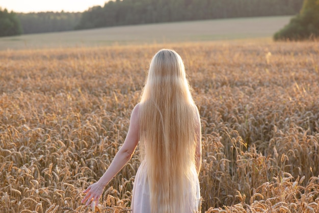 Ragazza bionda torna con i capelli lunghi sul campo di grano Soft focus