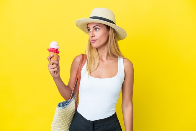 Ragazza bionda uruguaiana in estate con gelato isolato su sfondo giallo che guarda al lato