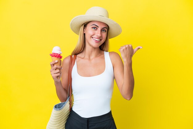 Ragazza bionda uruguaiana in estate con gelato isolato su sfondo giallo che indica il lato per presentare un prodotto