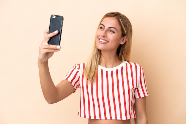 Ragazza bionda uruguaiana isolata su fondo beige che fa un selfie