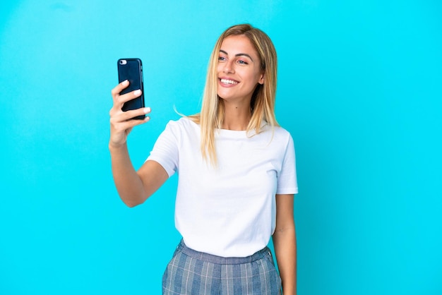Ragazza bionda uruguaiana isolata su sfondo blu che fa un selfie