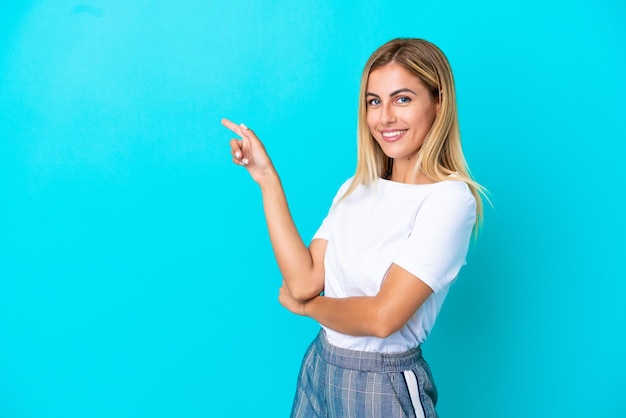 Ragazza bionda uruguaiana isolata su sfondo blu che punta il dito di lato