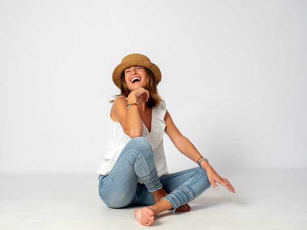 Ragazza bionda vestita in jeans, camicia bianca e un cappello seduto sul pavimento