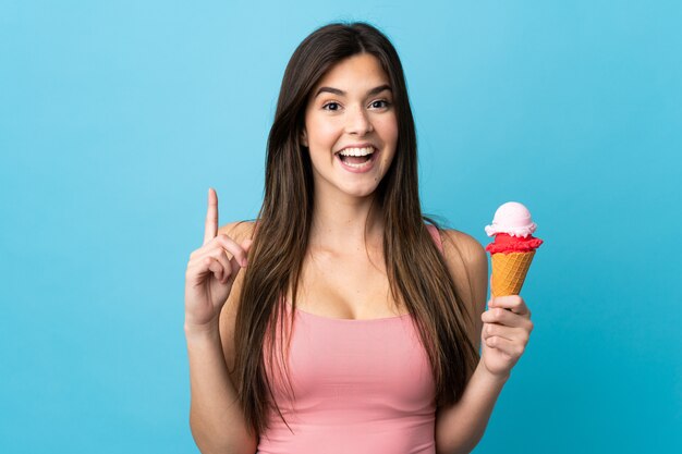 Ragazza brasiliana dell'adolescente che tiene un gelato della cornetta sopra la parete blu isolata che indica su una grande idea