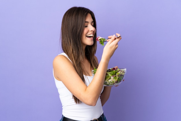 Ragazza brasiliana dell'adolescente che tiene un'insalata sopra la parete viola isolata