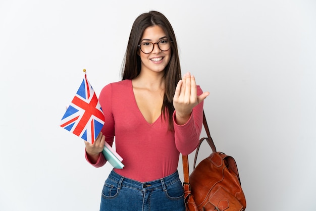 Ragazza brasiliana dell'adolescente che tiene una bandiera del Regno Unito isolata su bianco che invita a venire con la mano