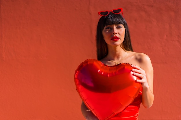 Ragazza bruna caucasica con palloncini cuore su sfondo rosso di San Valentino Posa di un modello