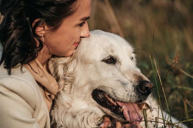 ragazza bruna che abbraccia il golden retriever bianco nel campo