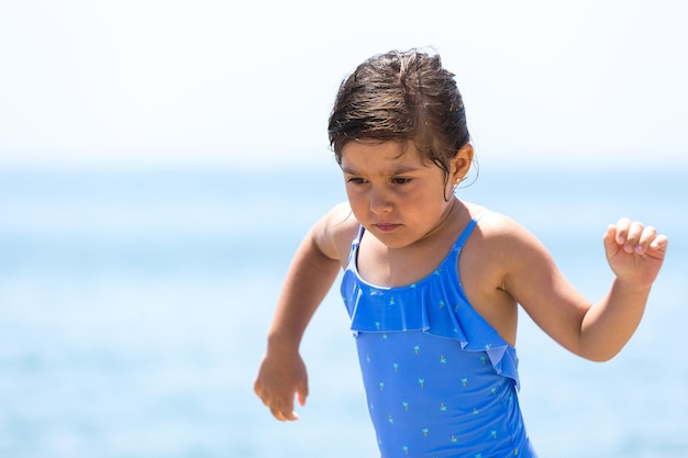 Ragazza bruna che indossa un costume da bagno sulla spiaggia in esecuzione con il cielo sullo sfondo Concetto di vacanza al mare protezione solare mare stile di vita e relax