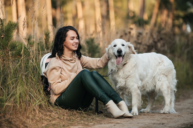 ragazza bruna con cane golden retriever bianco sulla strada forestale