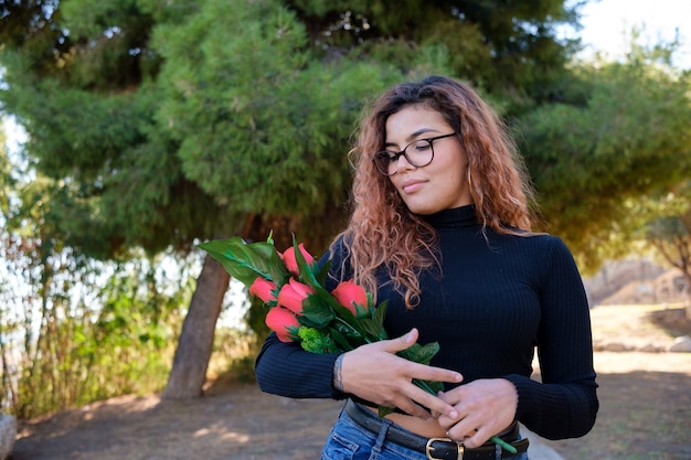 Ragazza bruna latina in trench grigio con rose rosse in mano