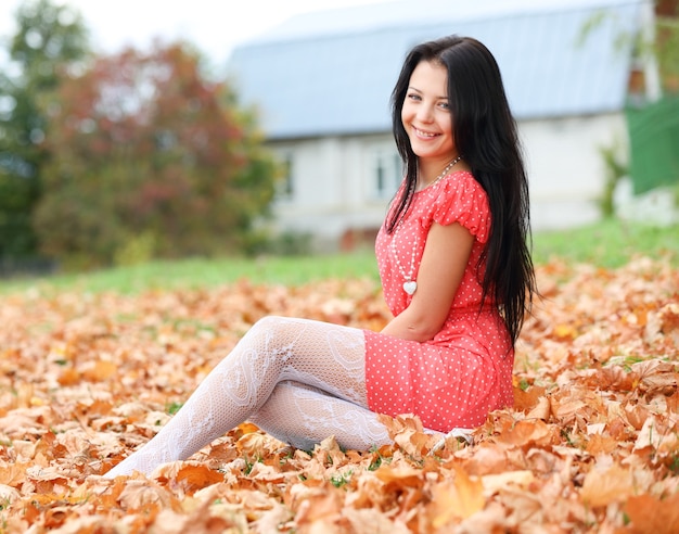 Ragazza bruna seduta sulle foglie d'autunno